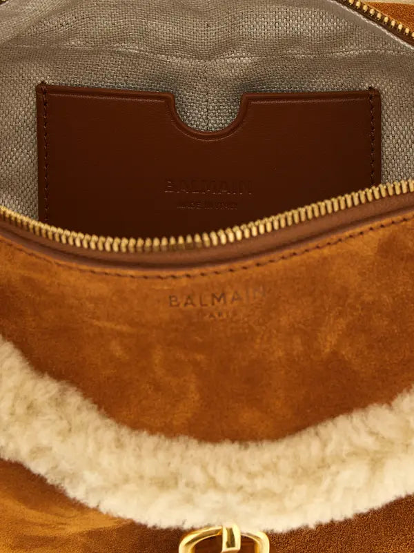 Close-up of a Balmain brown suede and shearling bag interior, showing a brown leather card holder with the Balmain logo, a gold zipper, and a cream shearling lining.