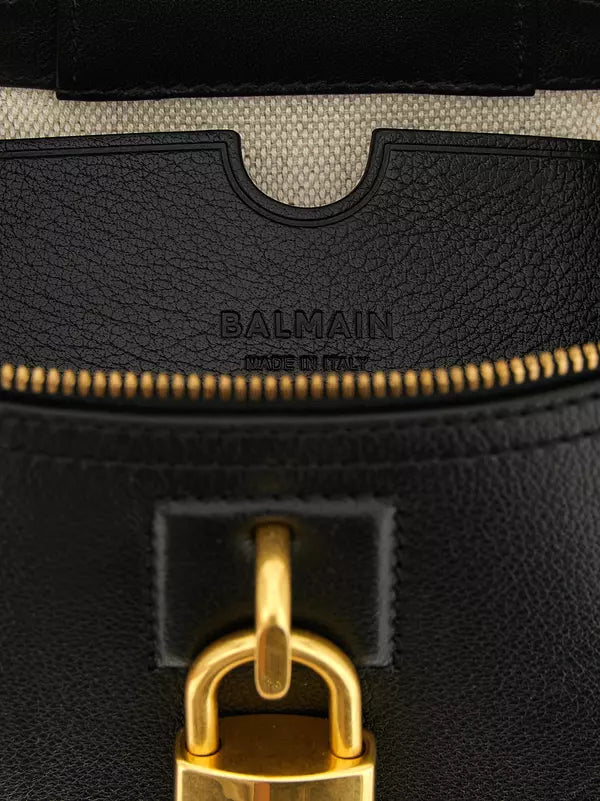 Close-up of a black textured leather and canvas handbag showing the interior, a gold zipper, and a gold padlock closure. The brand name &