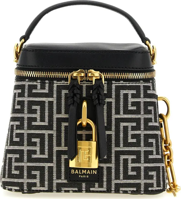 A Balmain Paris top-handle handbag featuring a black and white geometric monogram pattern, a black leather top panel, a gold padlock charm, and gold hardware.