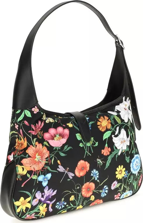 A black shoulder bag with a vibrant multicolor floral print, featuring a single black leather shoulder strap and a black leather trim.