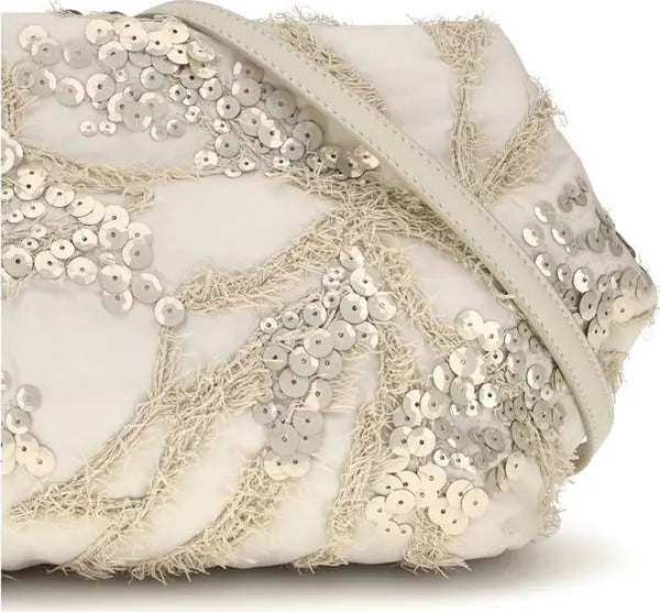 A close-up of a white evening clutch bag decorated with silver sequins and frayed beige tassel trim, featuring a light beige shoulder strap.