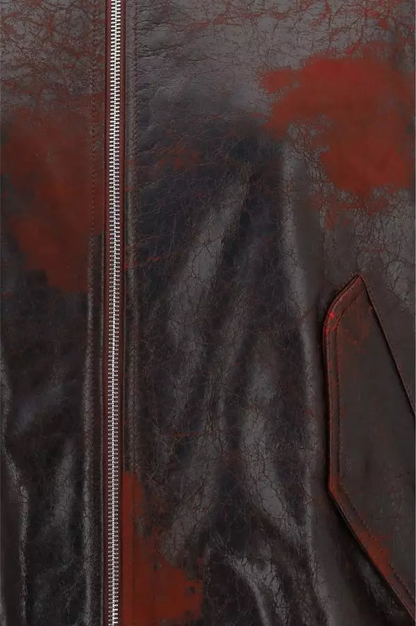Close-up of a dark brown leather jacket with a distressed red paint-splatter pattern and a silver zipper.