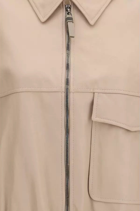 Close-up of a light beige or cream-colored jacket featuring a silver metal zipper, a pointed collar, and a stitched flap pocket on the right side.