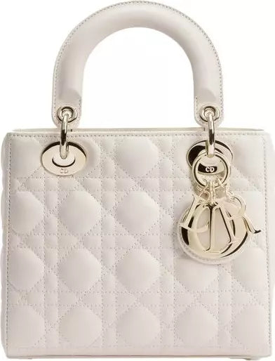 A white quilted leather top-handle handbag with silver-tone hardware, featuring a diamond-quilted pattern and a hanging charm on a plain white background.