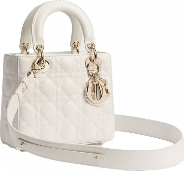 A white quilted leather handbag with gold-tone hardware, featuring dual top handles, a detachable shoulder strap, and a hanging charm on a plain white background.