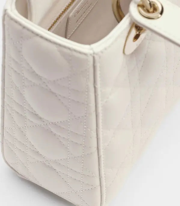 Close-up of a quilted cream-colored handbag with gold-tone hardware and a visible zipper inside the open top.