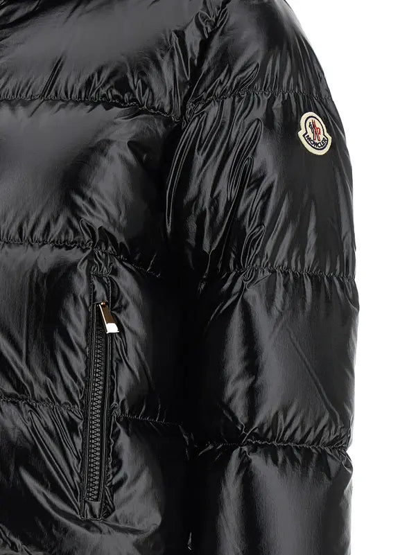 Close-up of a black puffer jacket showing horizontal quilting, a zippered pocket, and the circular embroidered Moncler logo on the upper sleeve.