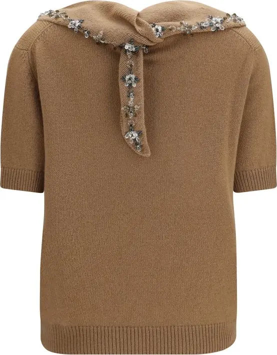A camel brown knit sweater featuring a wide collar adorned with a knotted bow and embellished with silver and white rhinestone floral details, set against a plain white background.