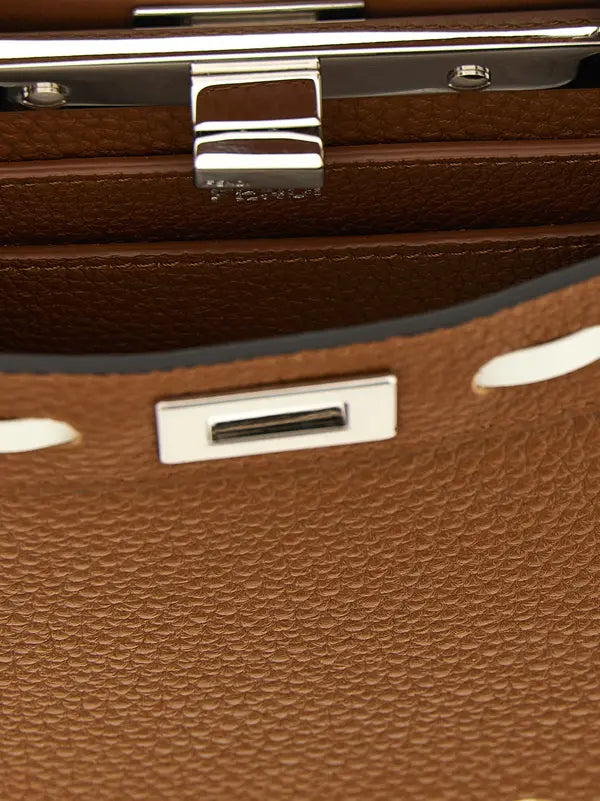 Close-up detail of a brown pebbled leather handbag showing silver-tone metal hardware, including a clasp engraved with &