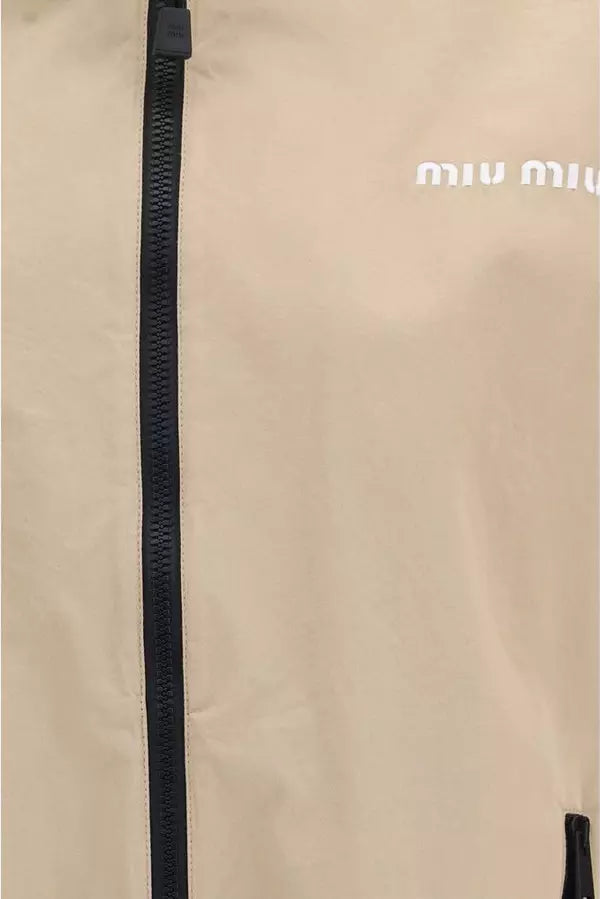 Close-up of a beige jacket with a black zipper and white Miu Miu logo on the chest.