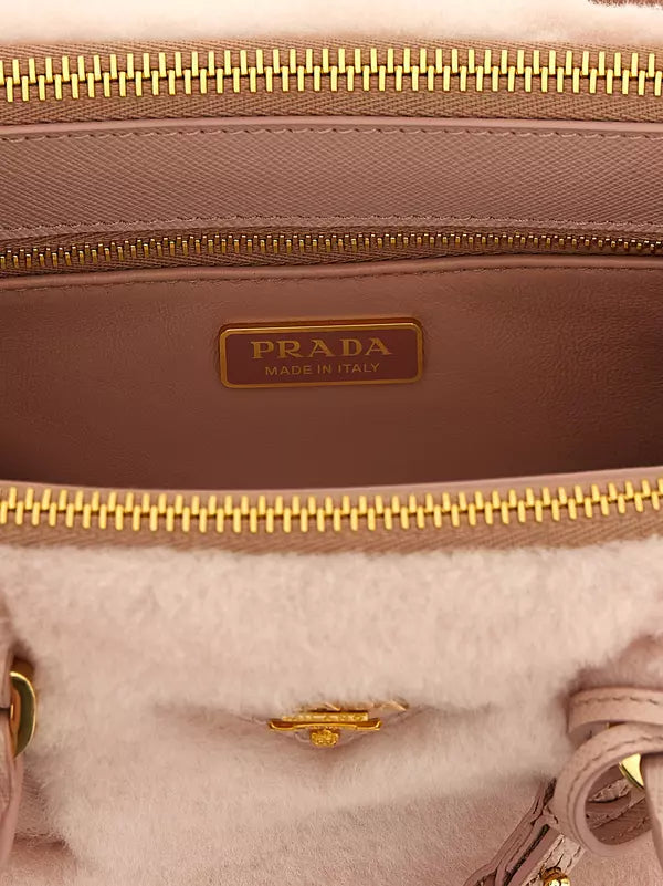 Close-up of a Prada handbag interior showing a taupe leather lining with a gold-tone Prada logo plaque, gold zipper, and a soft off-white faux fur lining.