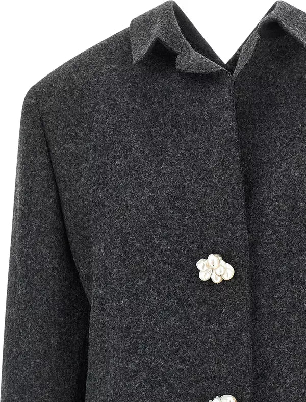 Close-up of a dark charcoal gray wool coat with a pointed collar and decorative white flower-shaped buttons.