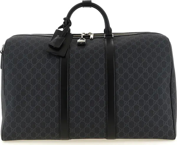 A black Gucci duffel bag featuring the signature GG monogram canvas, black leather trim, top handles, and a matching leather luggage tag with a silver padlock.