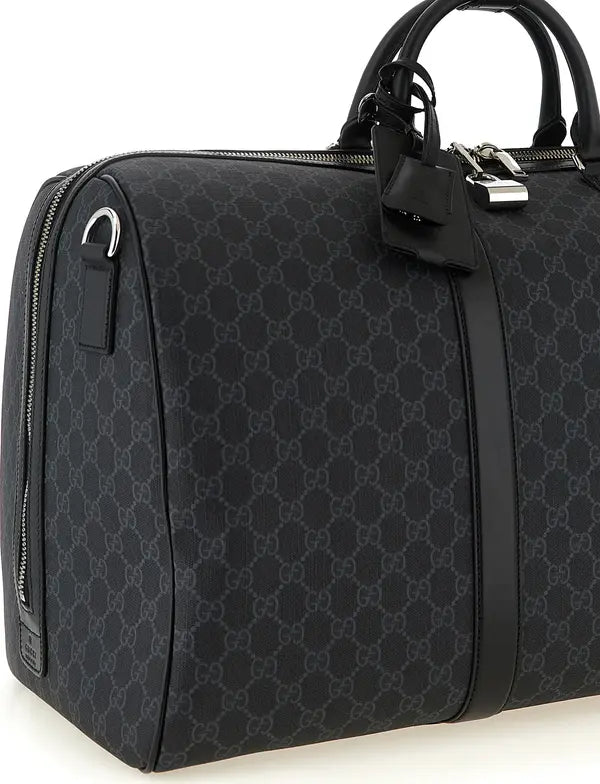 A black Gucci duffel bag featuring the signature GG monogram canvas, black leather trim, dual top handles, and a silver-toned lock and key on the front.