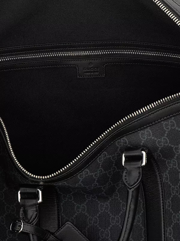 Close-up of the interior of a black Gucci duffel bag, showing the black fabric lining, silver zipper, and a small Gucci logo patch on the inside. The exterior pattern is partially visible at the bottom right.