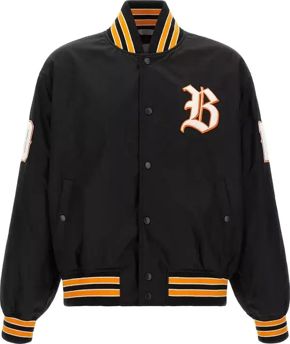 A black varsity-style bomber jacket with orange and yellow striped ribbed trim on the collar, cuffs, and hem, featuring a large embroidered gothic letter 'B' on the left chest.