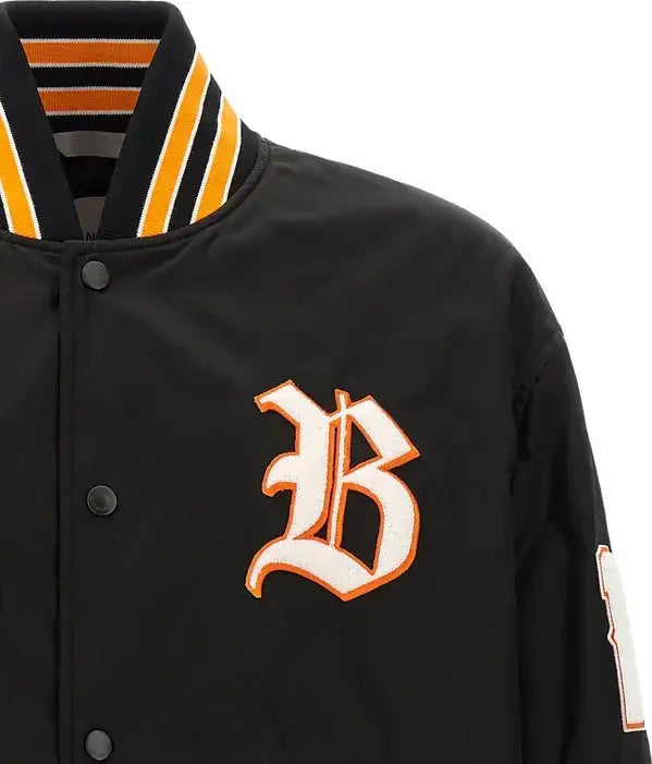 Close-up of a black varsity-style jacket with a striped navy, white, and orange collar, featuring a large white and orange embroidered letter &