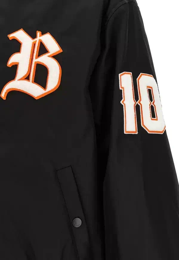 Close-up of a black varsity-style jacket sleeve featuring a large white and orange outlined letter &