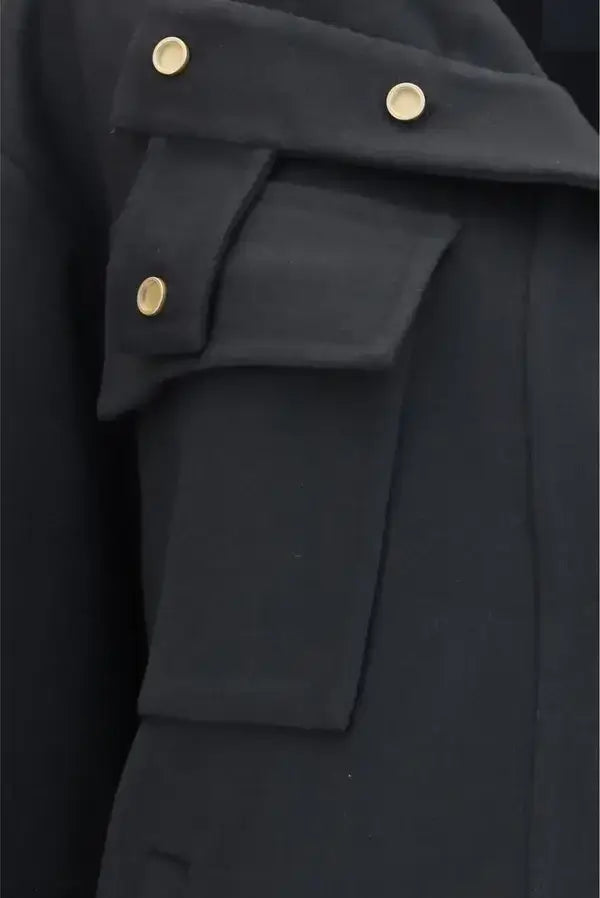 Close-up of a dark coat or jacket detail showing a flap pocket with gold-tone snap buttons and a structured lapel.