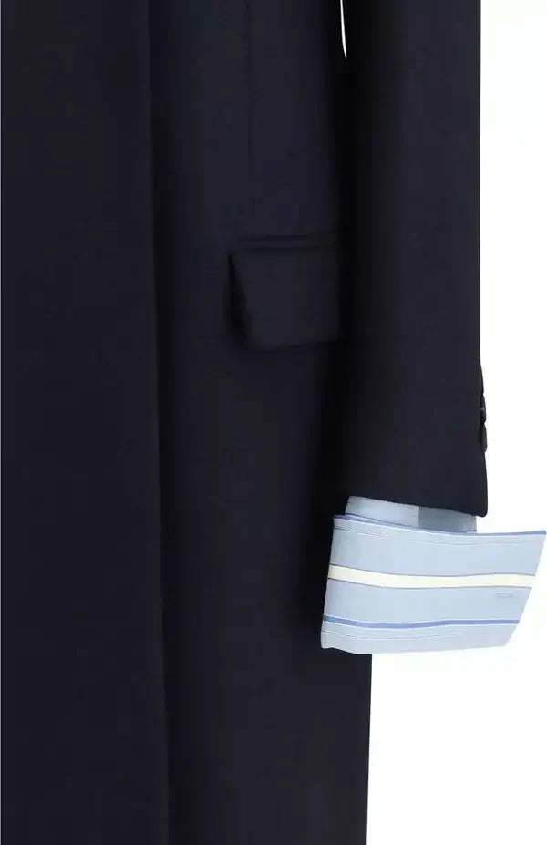 Close-up of a dark navy coat sleeve with a light blue and white striped dress shirt cuff peeking out, set against a plain white background.