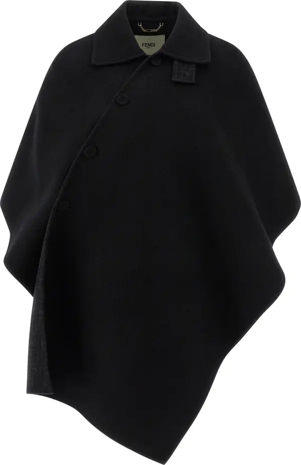 A black asymmetrical cape-style coat with a pointed collar, front buttons, and a small square patch detail on the chest, shown on a plain white background.