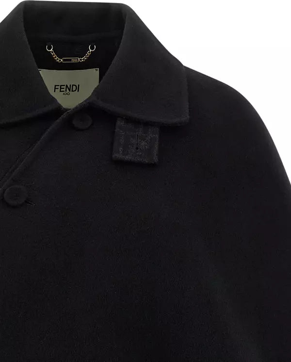 Close-up of a black Fendi cape coat featuring a structured collar, a single button closure, and a woven Fendi logo patch on the collar.