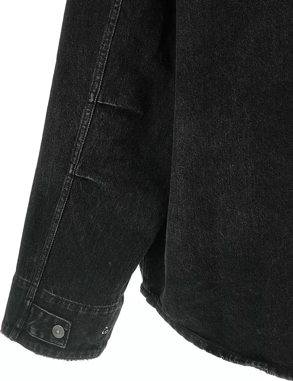 Close-up detail of a black denim jacket sleeve with a buttoned cuff, showing the dark washed fabric texture and seam lines against a white background.