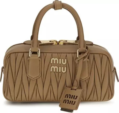 A Miu Miu mini top-handle bag in tan leather with a distinctive chevron quilted pattern and gold-tone hardware, shown against a plain white background.