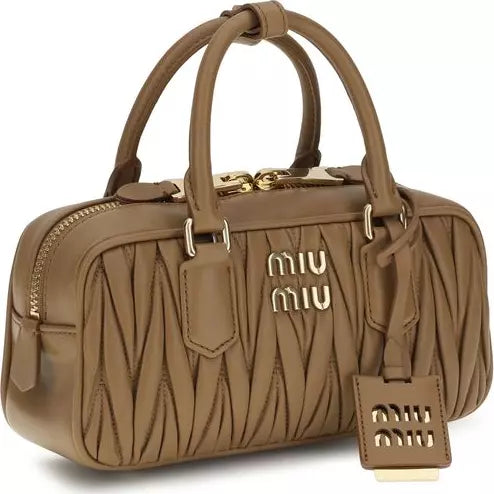A Miu Miu taupe brown leather handbag with a distinctive wavy quilted pattern, gold-tone hardware, and the brand's signature logo on the front and hanging tag.