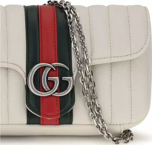 A close-up of a Gucci shoulder bag in off-white leather with the signature green and red web stripe and a silver-tone GG logo on the front flap, with part of the silver chain strap visible.