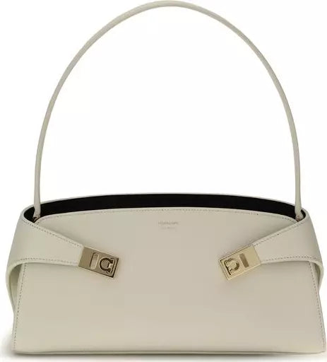 An off-white leather shoulder bag with a curved top handle, gold-tone hardware, and a black interior lining, shown against a plain white background.