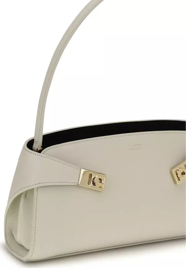 A close-up of a light beige leather handbag with gold-tone hardware and a black interior lining, shown against a plain white background.