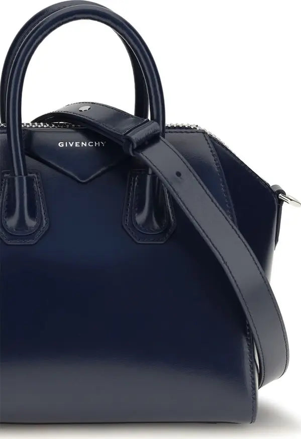 A navy blue Givenchy handbag with a glossy finish, featuring dual top handles, a shoulder strap, and silver-tone hardware on a white background.