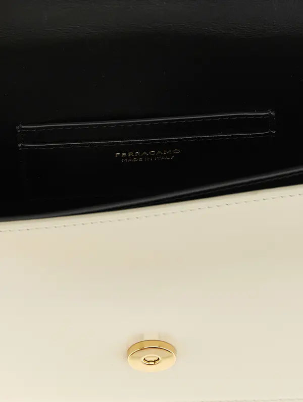 Close-up detail of a Ferragamo handbag showing a black leather interior pocket with the brand name embossed, a white leather exterior flap, and a gold-tone snap button closure.
