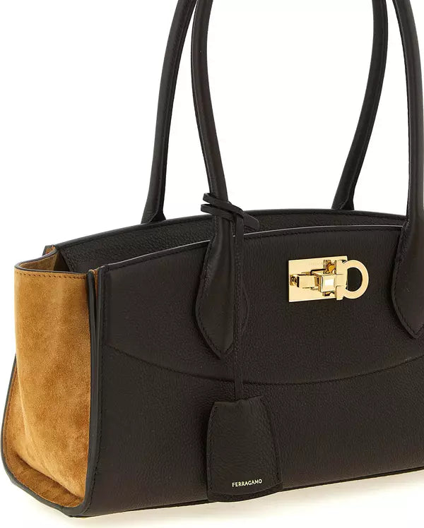 A black leather handbag with a tan suede side panel, gold-tone hardware, and double shoulder straps, photographed on a clean white background.