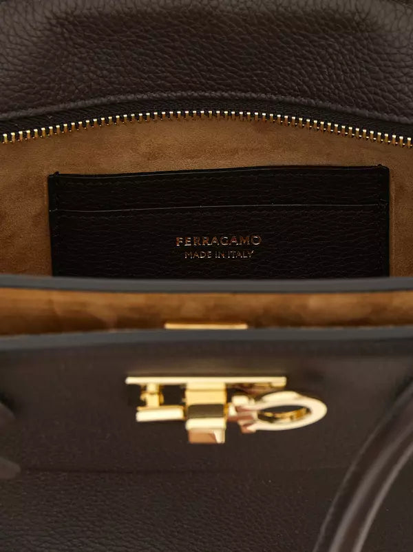 Close-up of the interior of a dark brown leather handbag, showing a black leather interior label with gold lettering that reads &