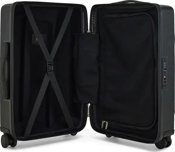 An open hard-shell suitcase shown from the inside, revealing a black interior with a compression strap, zippered pocket, and storage compartment.