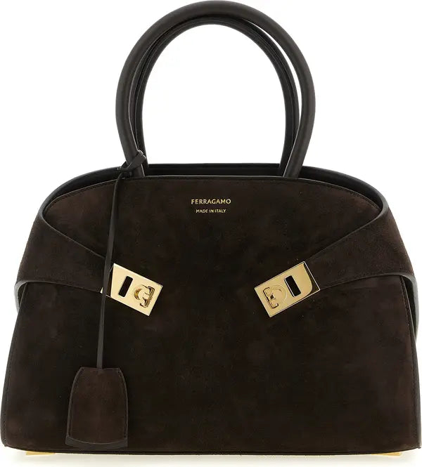 A dark brown suede handbag by Ferragamo with gold-tone hardware and double top handles, shown against a plain white background.