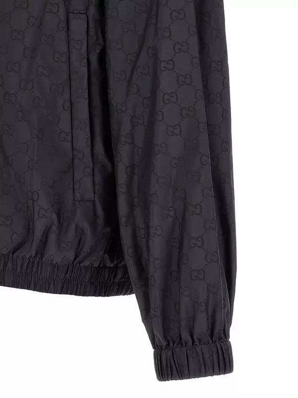 Close-up of a black long-sleeve jacket with an allover tonal GG monogram pattern, elasticized hem, and gathered cuffs, shown against a white background.