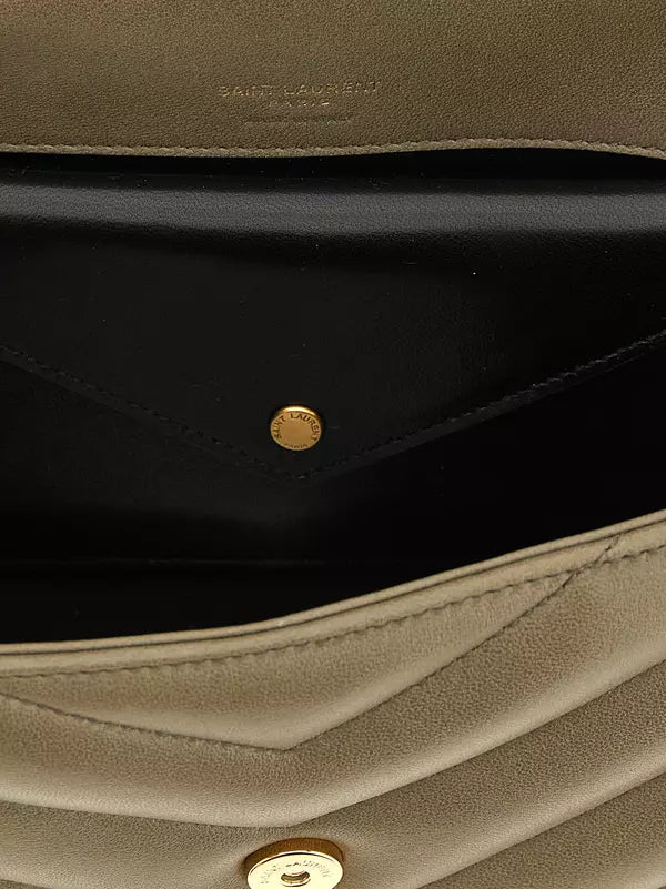 Close-up of the interior of a Saint Laurent handbag, showing a black leather pocket with a gold-tone snap button and a taupe leather exterior.