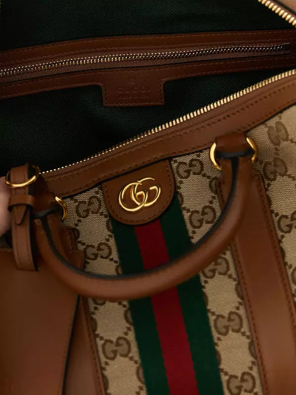 Close-up of a Gucci handbag showing the interior, brown leather trim, gold-tone hardware, and the signature GG monogram canvas with the green and red web stripe.