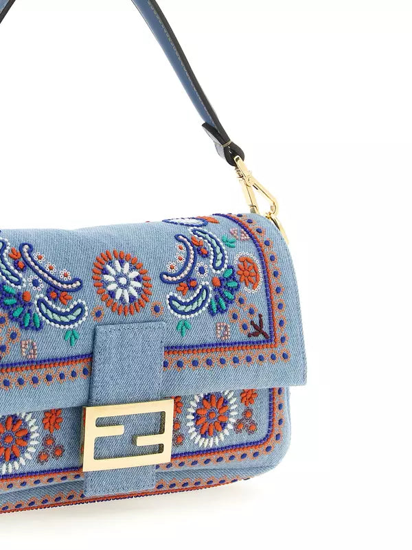 A close-up of a light blue denim shoulder bag featuring intricate multicolor embroidered paisley and floral patterns, a gold-tone Fendi FF logo clasp, and a dark blue strap with gold hardware.
