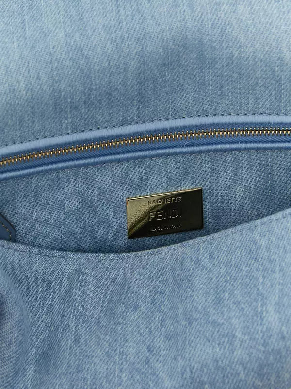 Close-up of a light blue denim or canvas bag interior with a gold-tone zipper and a small metallic brand plaque reading Fendi.