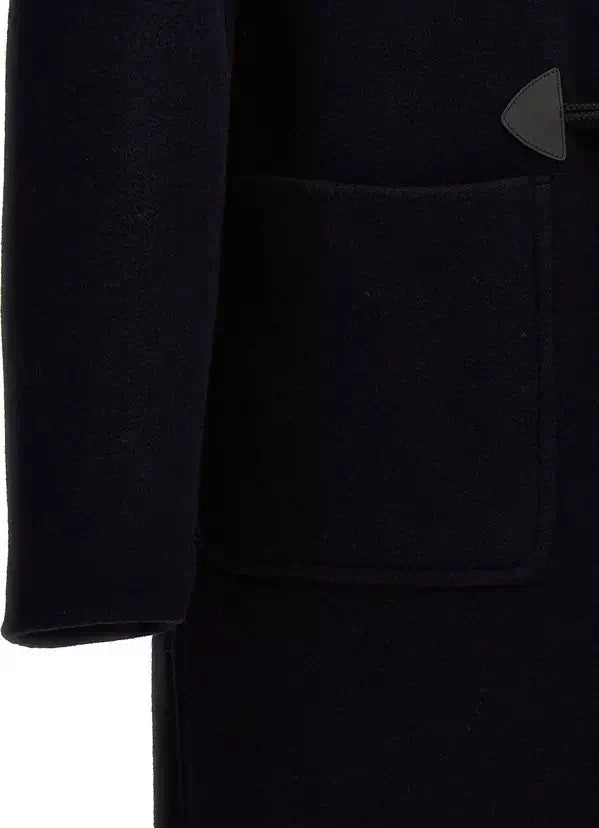 Close-up of a black wool coat featuring a large front patch pocket and a dark triangular leather brand tab on the upper right side.