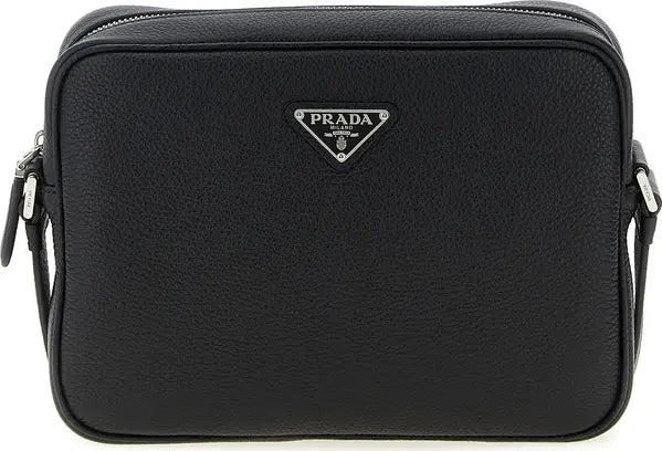 A black Prada pebbled leather camera bag with a silver-tone triangular logo plaque on the front, set against a plain white background.