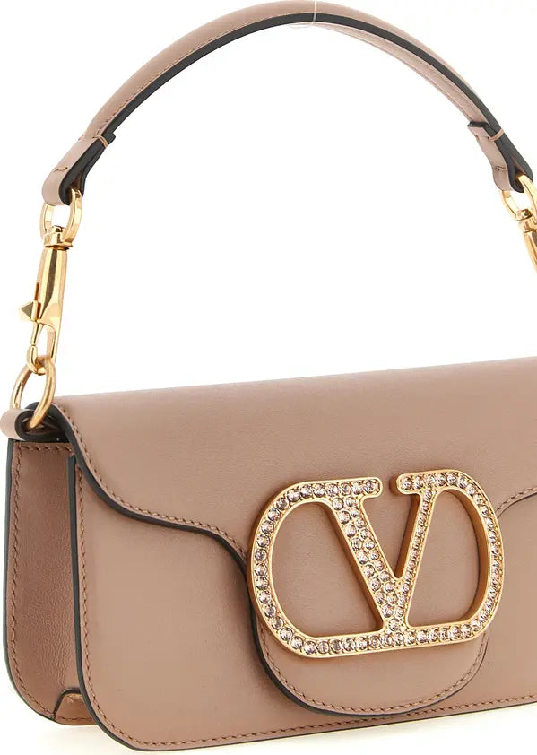 A close-up of a taupe leather handbag featuring a large gold-tone &