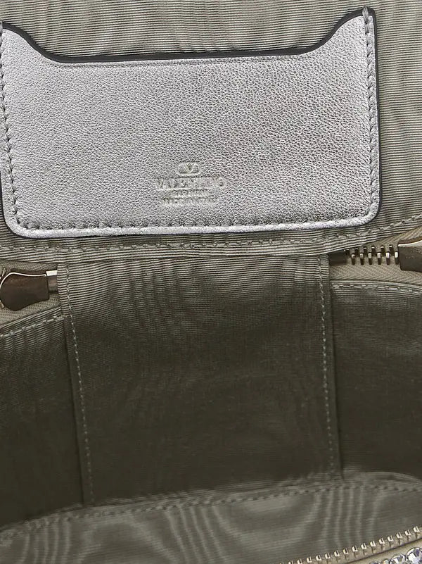 Close-up of the interior of a Coach handbag, showing a silver-tone textured leather brand patch with the Coach logo and name, stitched onto an olive green nylon fabric lining.