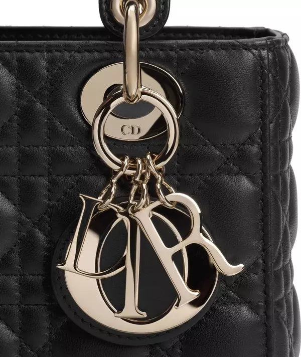 Close-up of a black quilted leather handbag charm featuring a large polished silver-tone Dior logo keychain and a circular Dior logo medallion.