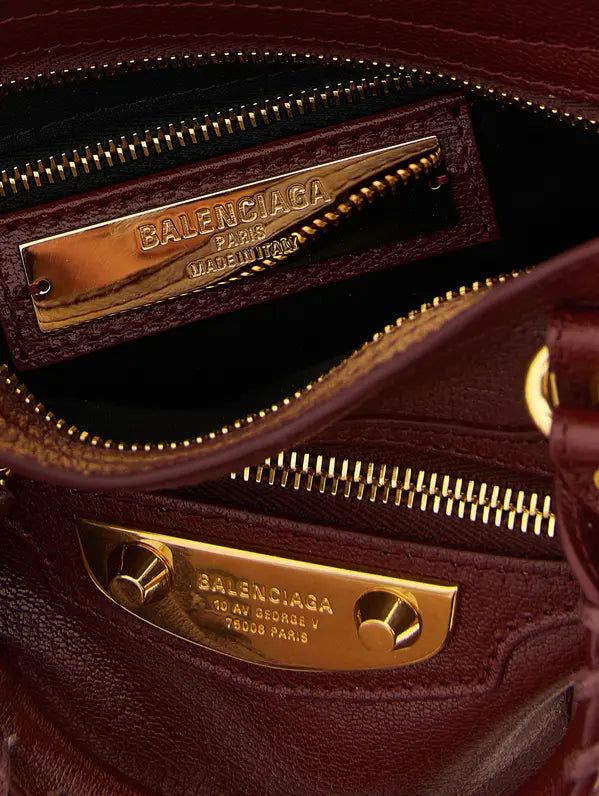 Close-up of a Balenciaga handbag interior showing a burgundy leather compartment with gold-tone hardware and a visible Balenciaga Paris metal plaque.