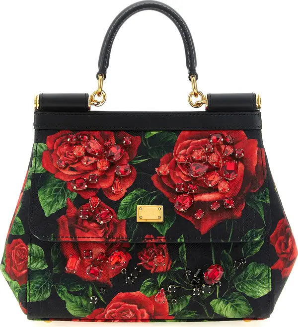 A structured black handbag with a red rose and green leaf print, embellished with red crystal-like beads and a gold-tone front clasp, shown on a plain white background.